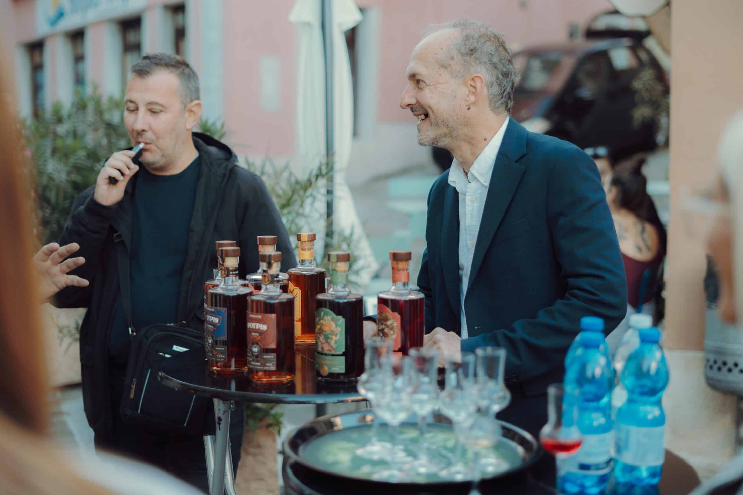 High-quality alt text describing NDV Rakija bottles at outdoor tasting event for SEO.