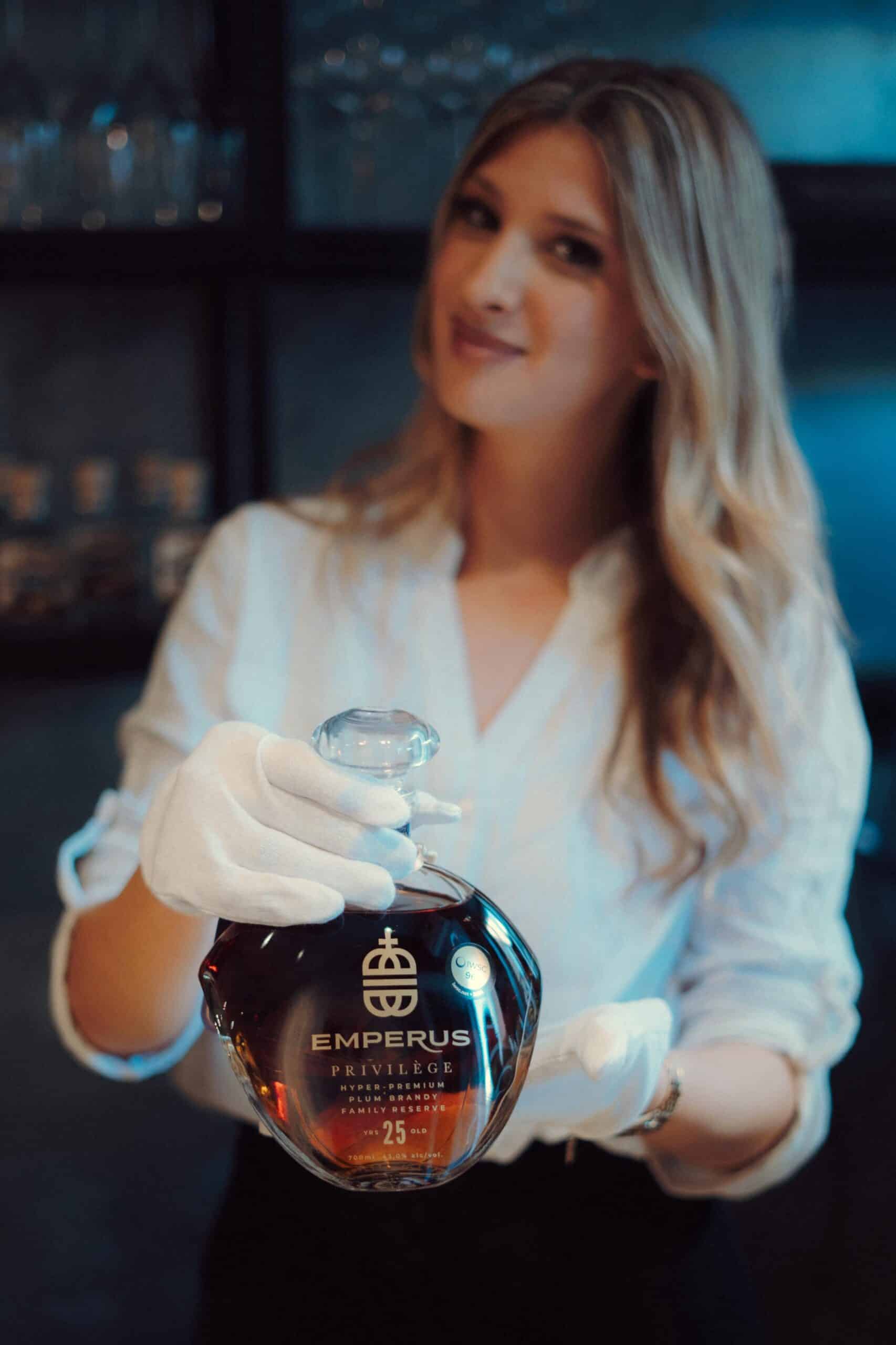 Image of a woman holding a bottle of NDV Rakija in a stylish setting, emphasizing premium quality and traditional distillation.
