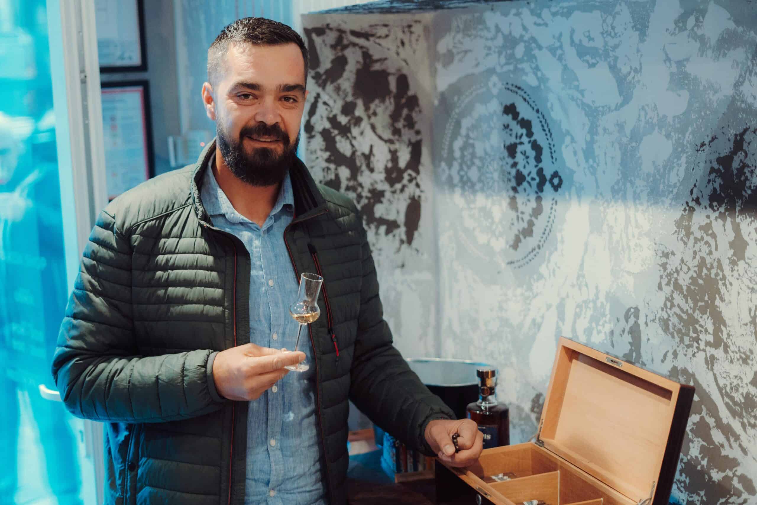 Alto text: Man holding a glass of traditional rakija in a tasting room, showcasing NDV Rakija.