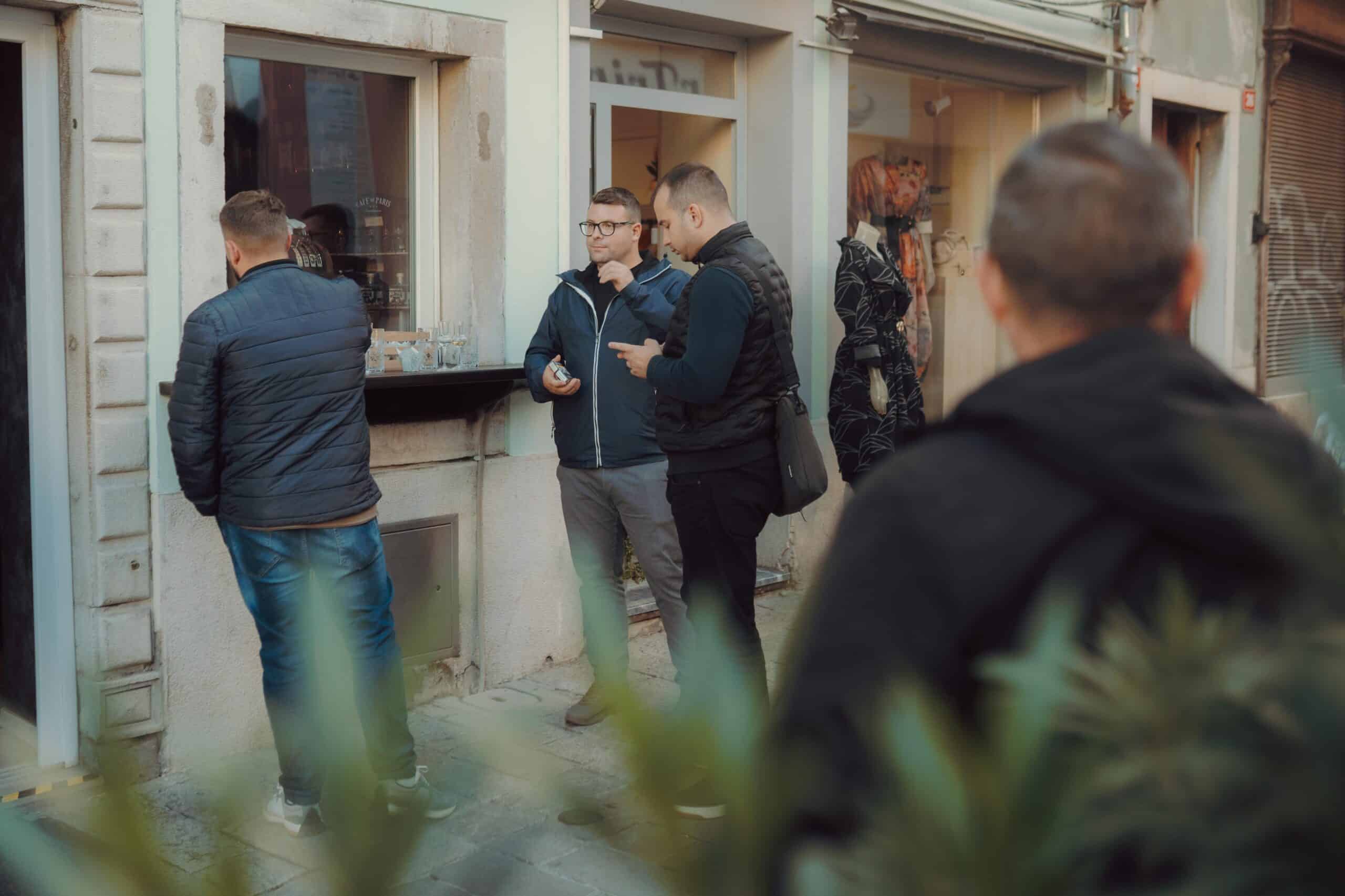 Alt: Men enjoying rakija outside a shop in Slovenia, traditional Balkan fruit brandy.