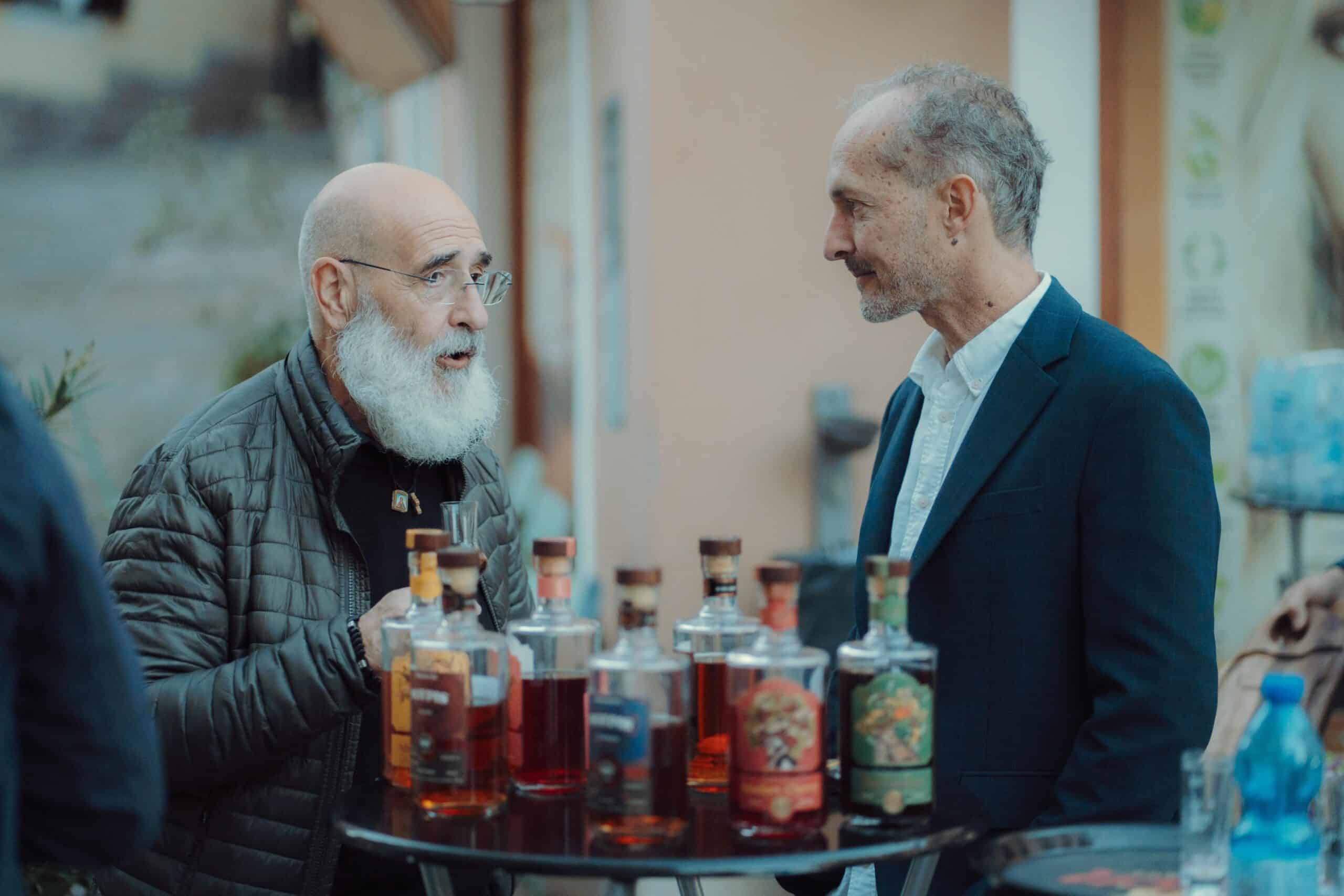 Alt text: Two men discussing rakija bottles at a tasting stand, showcasing NDV Rakija varieties.