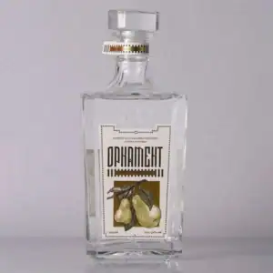Clear glass bottle of traditional rakija with pear illustration and elegant labeling.